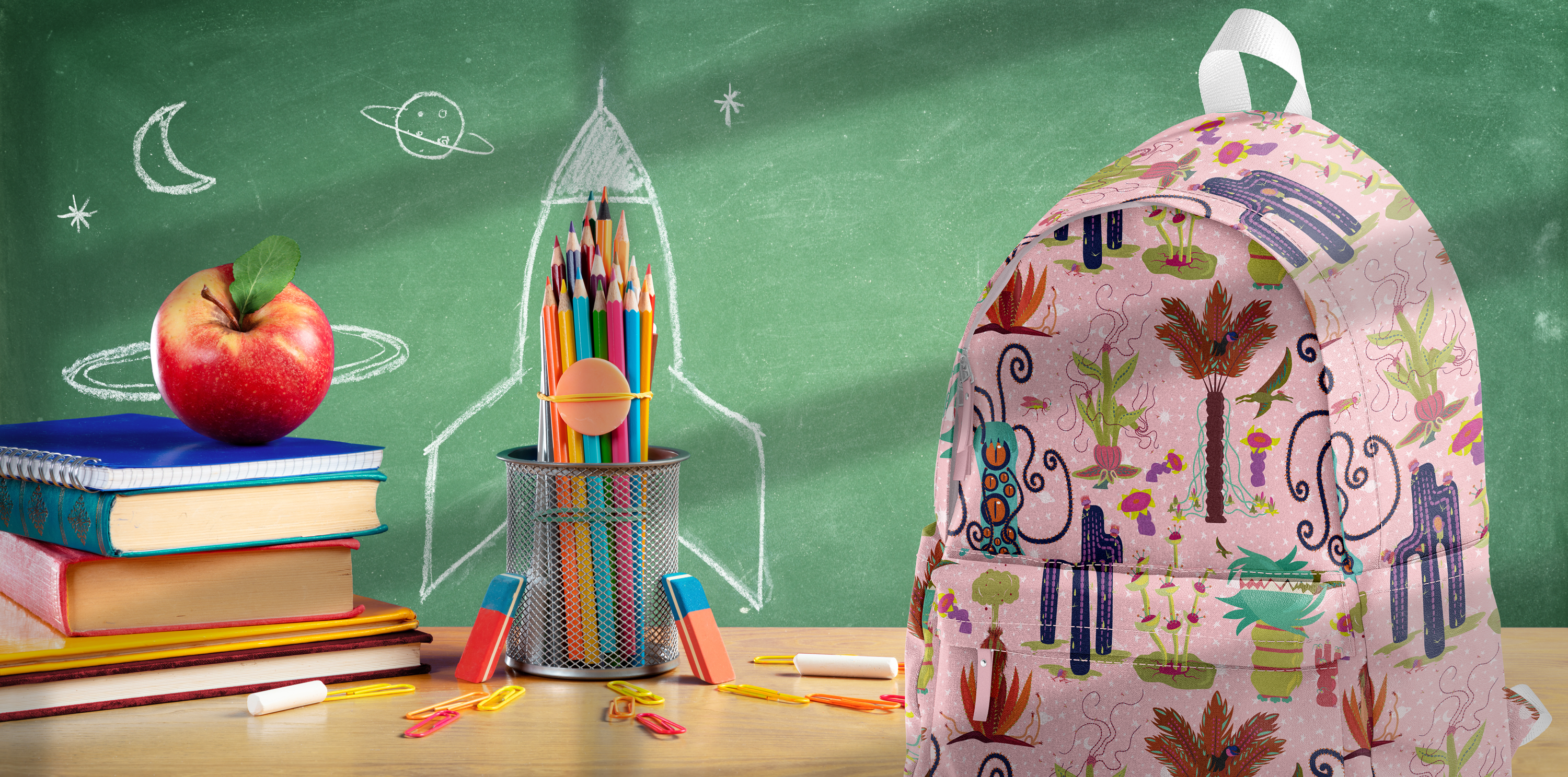 Image of a backpack featuring Seaweed & Spruce's Other Worldly "Creatures" pattern. The backpack is sitting on a desktop in front of a green chalkboard.
