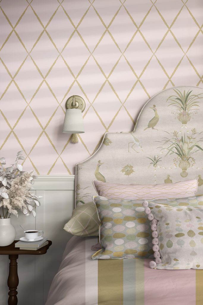 An image of a section of a bed with upholstered headboard, wallpaper and bedding all featuring patterns from the Sennen Collection in Blush. Suface pattern design.
