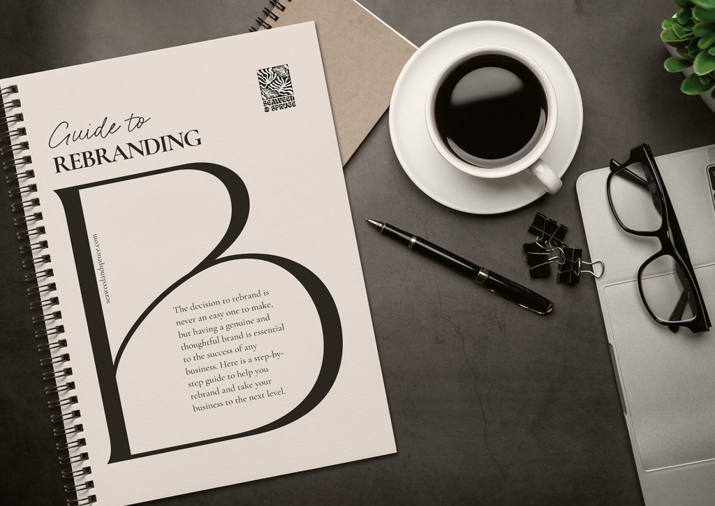 Image of a spiral ring binder on a dark desk which features a laptop (portion), spectacles, pen, notebook and a cup of coffee. The spiral ring binder's cover features Seaweed & Spruce's "Guide to Rebranding".