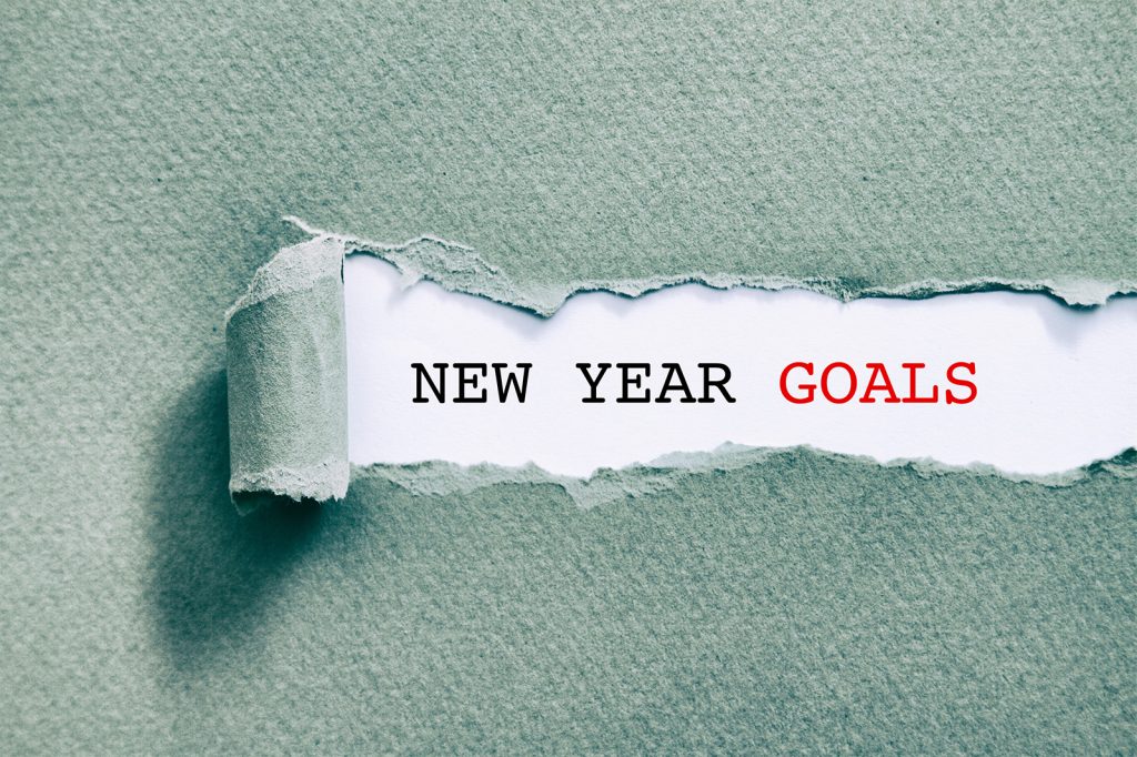 Image of a torn strip of teal-coloured paper revealing the typed words "New Year Goals" on a white background. The word "Goals" is in red. 2025