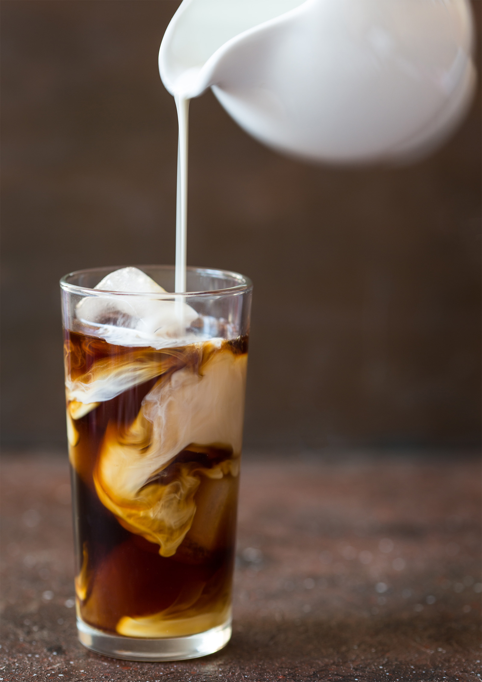Image of a tall glass filled with Salted Maple Cinnamon Cold Brew. Fresh cream is being slowly poured into the glass.