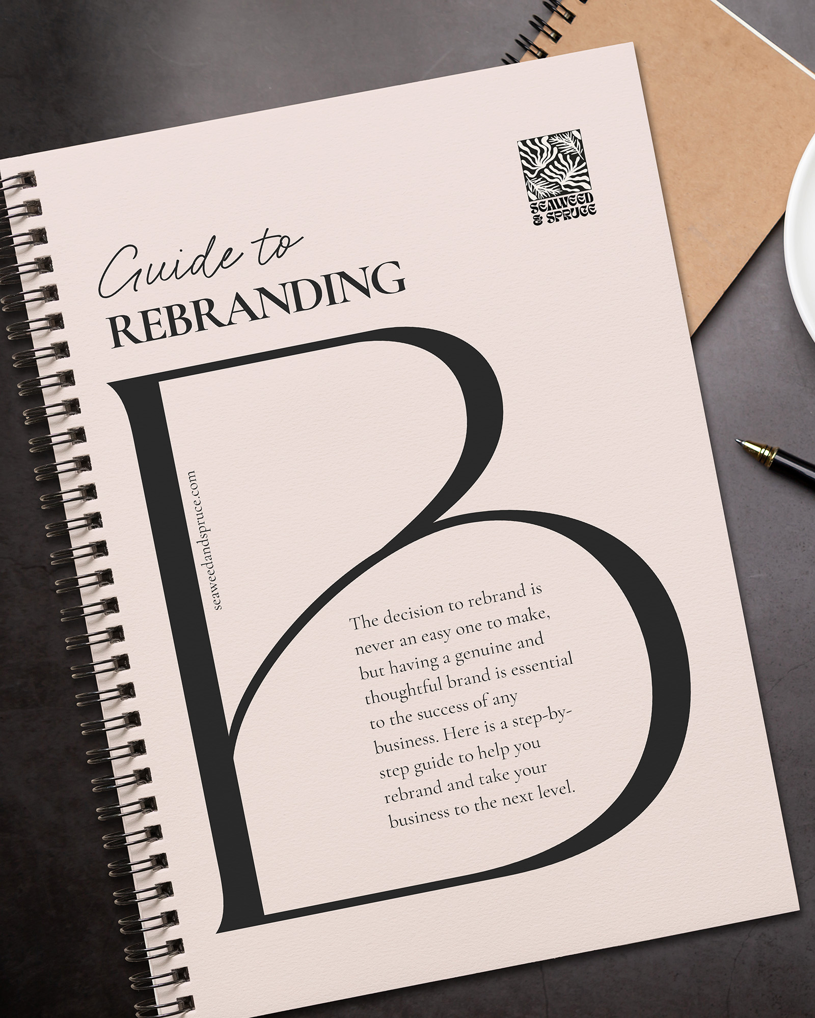 Image of a spiral ring binder on a dark desk. The spiral ring binder's cover features Seaweed & Spruce's "Guide to Rebranding".